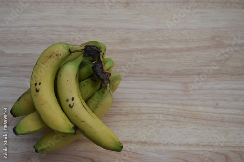 food photography image of fresh ripe yellow fruit bananas with drawn on smile for happy healthy living on natural light wood background with copy space