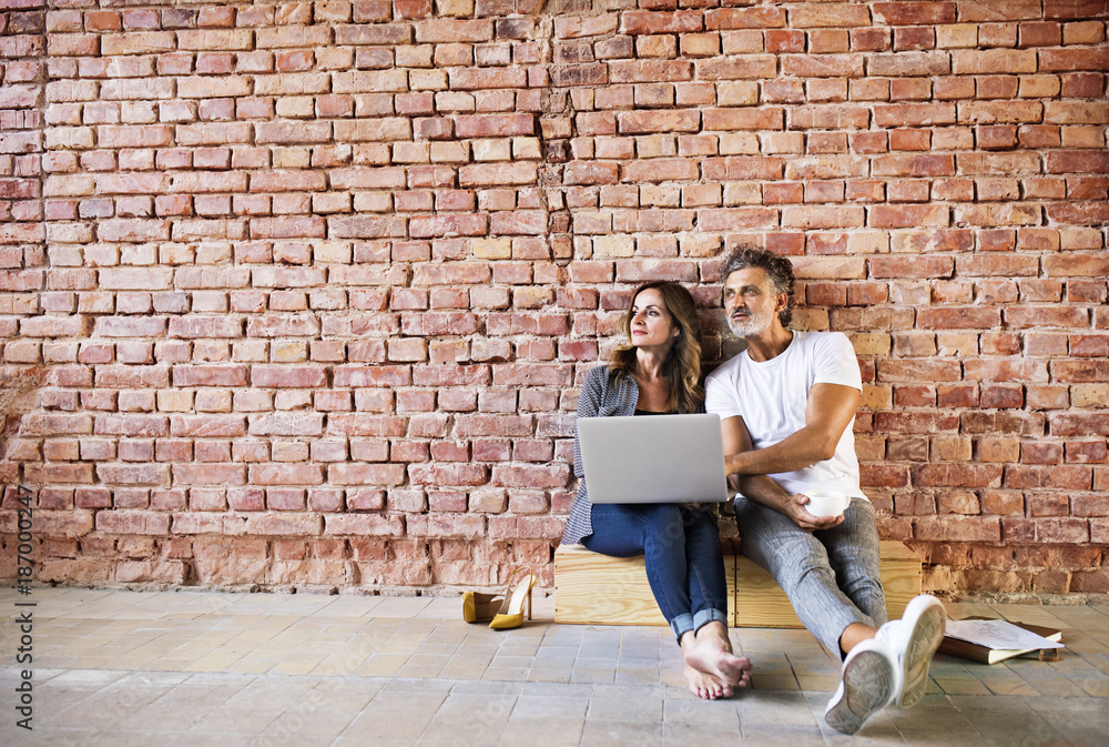 Businessman and woman sitting in a loft, using laptop, founding a start-up company Businessman and woman sitting in a loft, using laptop, founding a start-up company