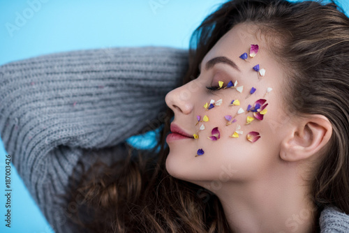 happy young woman with flowers on face in warm sweater isolated on blue