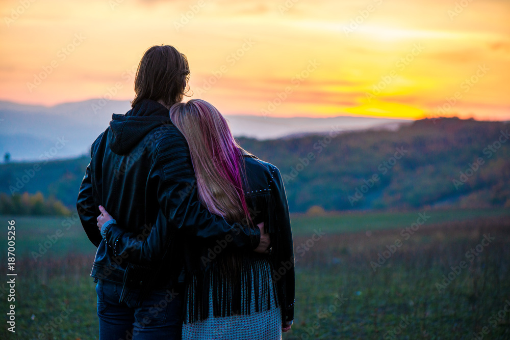 Lovely couple standing on top of the mountain, hugging and watching beautiful autumn sunset 