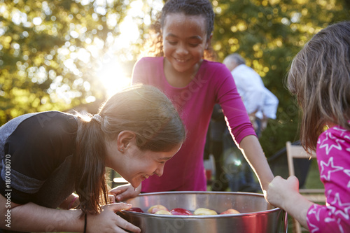 Young girls laugh while apple bobbing at a backyard party photo