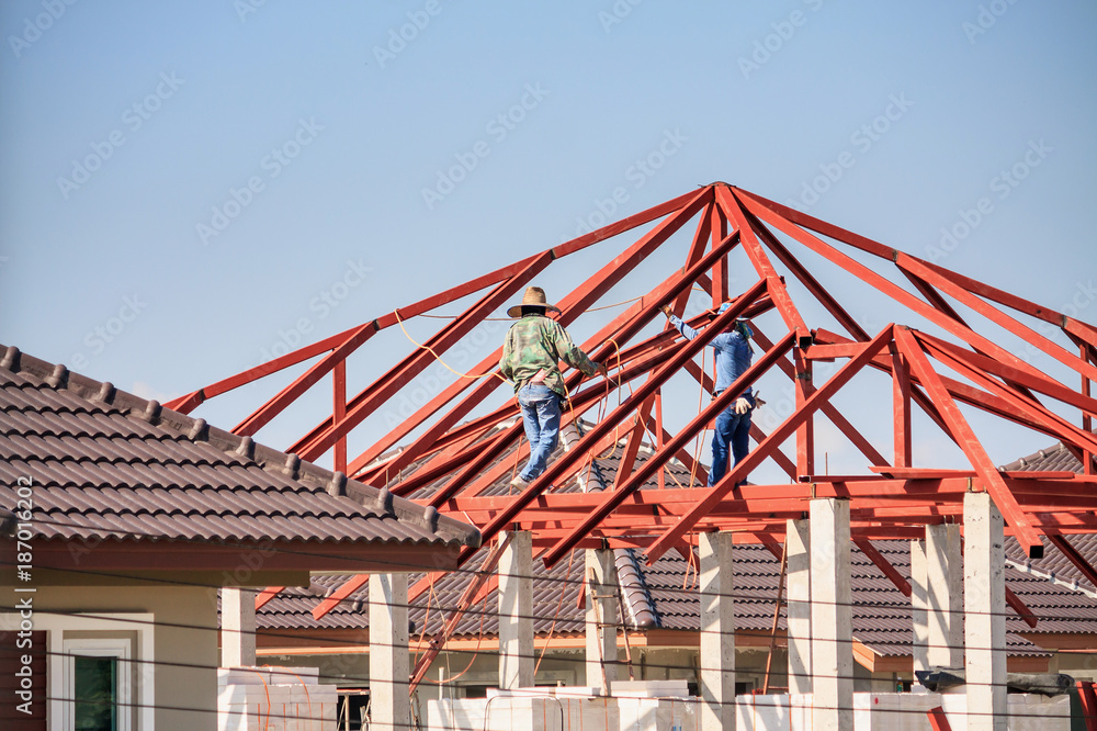 welder workers installing steel frame structure of the house roof at building construction site