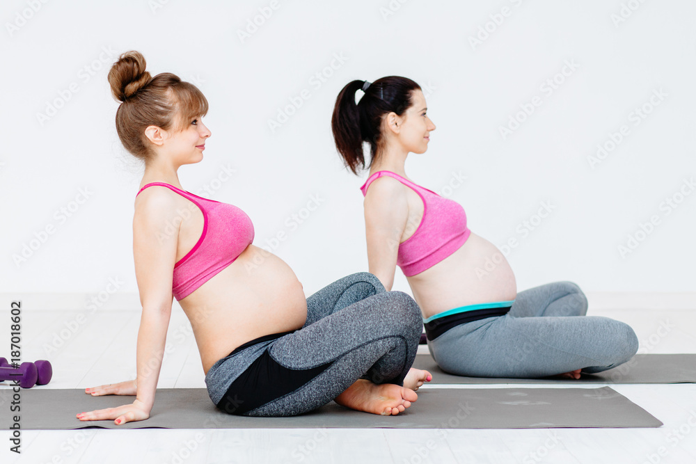 Group of two young pregnant women doing relaxation exercise on exercising mat. Sport, health, maternity and child concept. Group of two young pregnant women doing relaxation exercise on exercising mat. Sport, health, maternity and child concept.