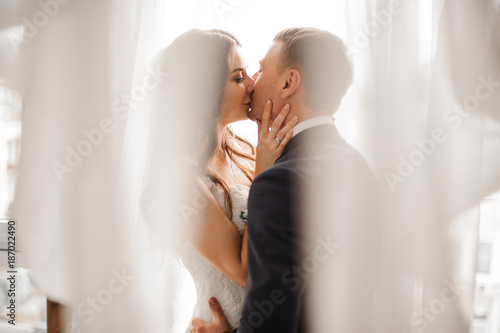 manly groom and beautiful bride kissing against white background