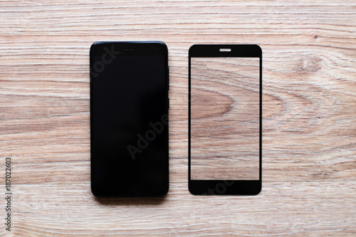 black phone and the protective glass on wooden background