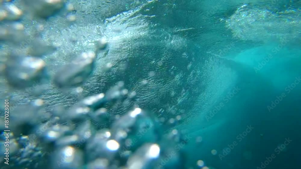 SLOW MOTION UNDERWATER: Crystal clear barrel wave breaking over camera in deep ocean. Camera descends from sunny beaches of Fuerteventura to deep crystal clear water below a large bubbling ocean wave.