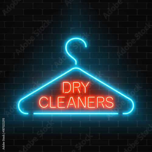 Neon dry cleaners glowing sign with hanger on a dark brick wall background.