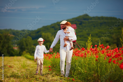 father and sons walking through the poppy flower field at summer day
