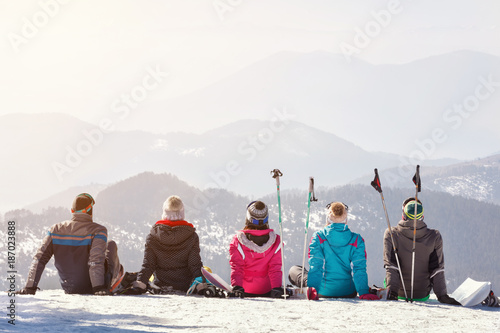 Skiers looking mountain's landscape while sitting on snow, back view