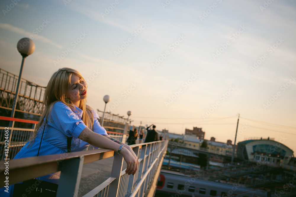 portrait of a cute young blond woman in a summer day against the background of a railway station