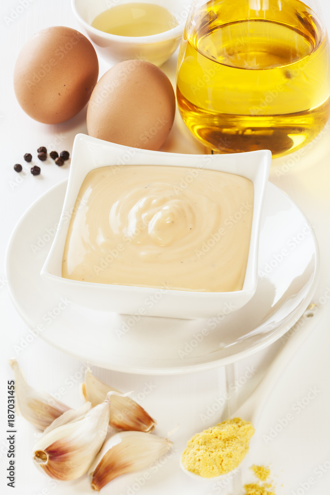 A bowl of homemade mayonnaise or aioli and its ingredients, oil, vinegar, eggs, black peppercorns, mustard and garlic. A bowl of homemade mayonnaise or aioli and its ingredients, oil, vinegar, eggs, black peppercorns, mustard and garlic.