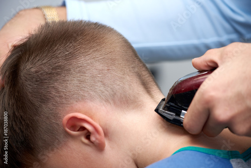 Barber is doing haircut to boy using hair clipper in barbershop.