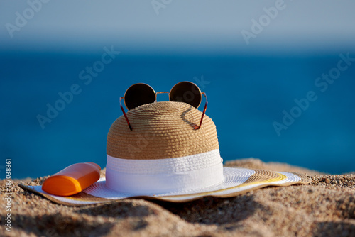 Bonnet hat, sunglasses and bottle of sunscreen on the beach sand.