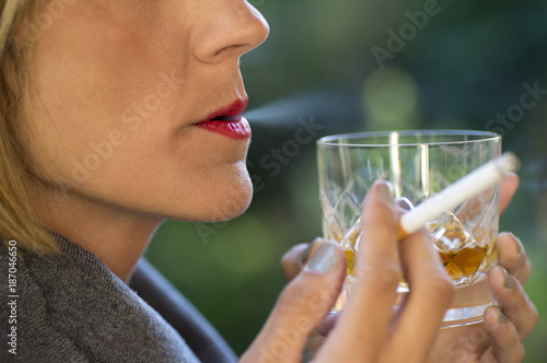 Beautiful lady drinking a glass of whiskey and smoking a cigarette