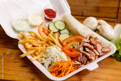 Shawarma sandwich - fresh roll of thin lavash (pita bread) filled with grilled meat, mushrooms, cheese, cabbage, carrots, sauce, green. Traditional Eastern snack. On a wooden background