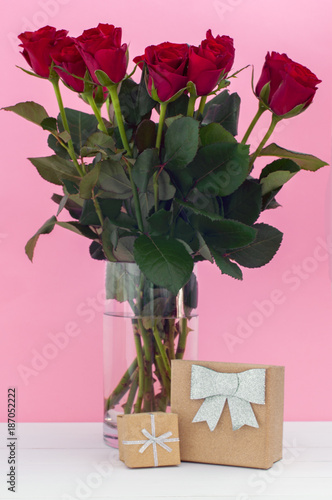 Beautiful red roses in a vase and gift glitter boxes on pink background