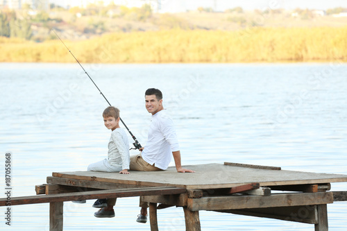 Father and his son fishing from pier on river