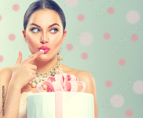 Funny joyful beauty model girl holding big beautiful party or birthday cake over green background and tasting it