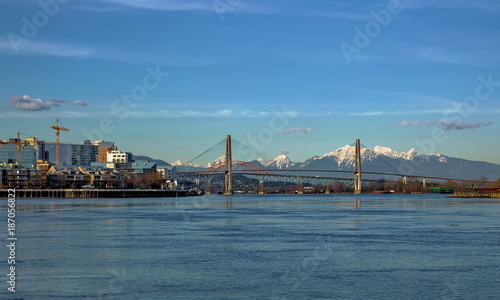 Residential District in New Westminster City with new construction at the waterfront of Fraser River and three bridges at the bakground of blue ske and snow caped mountain range 