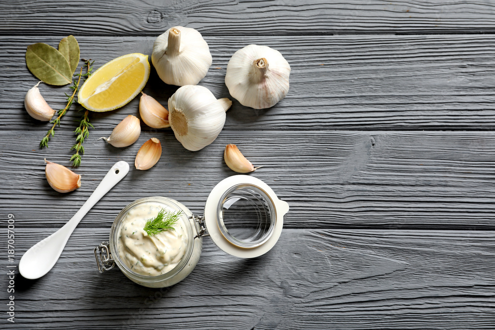 Tasty sauce with garlic in jar and ingredients on wooden table Tasty sauce with garlic in jar and ingredients on wooden table