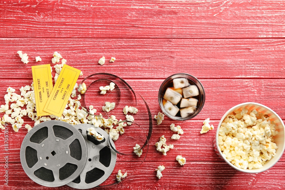 Tasty popcorn, tickets and movie reel on red wooden background