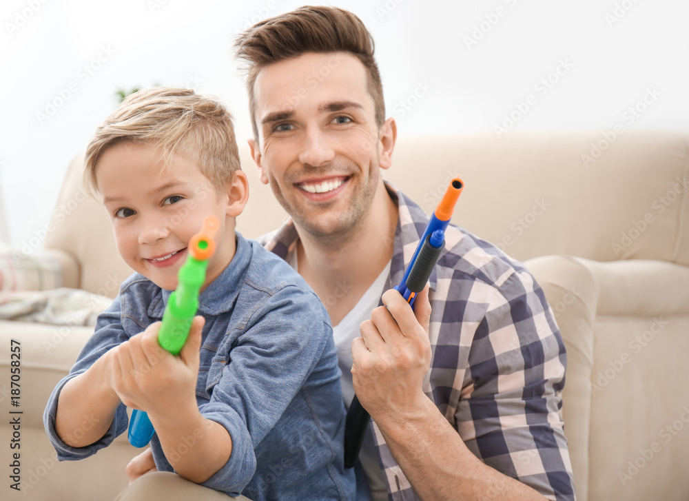 Cute boy and his father playing with toy guns at home Cute boy and his father playing with toy guns at home