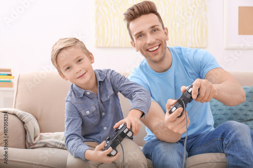 Cute boy and his father playing videogame at home