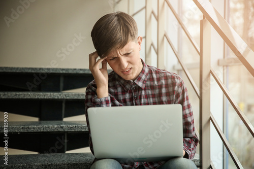 Upset teenage boy with lapt...
