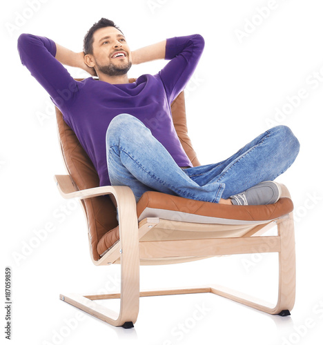 Handsome young man sitting in comfortable armchair on white background © Africa Studio