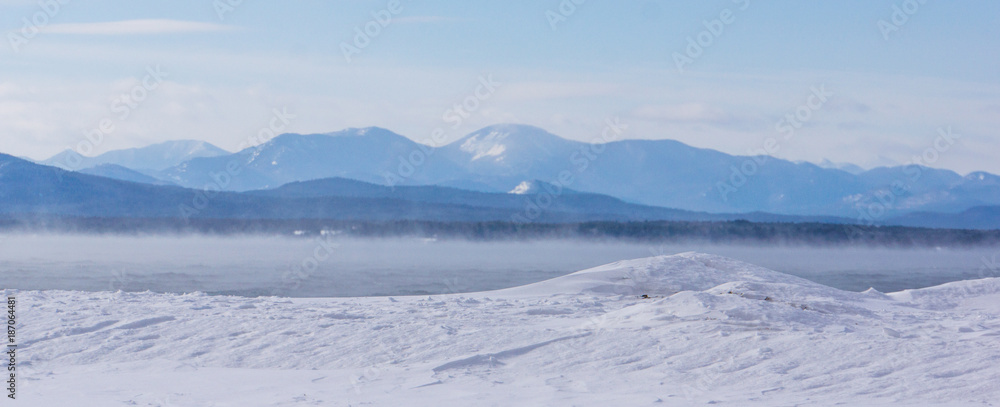 Fototapeta premium frigid winter morning with misty steam rising off the lake with the Adirondack mountains across the lake in New York 