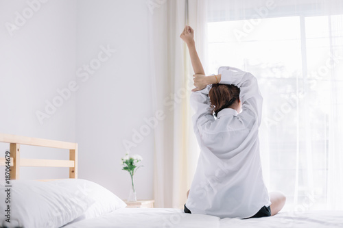 Happy woman stretching on bed after waking up in the early morning at window side. Have a good day.
