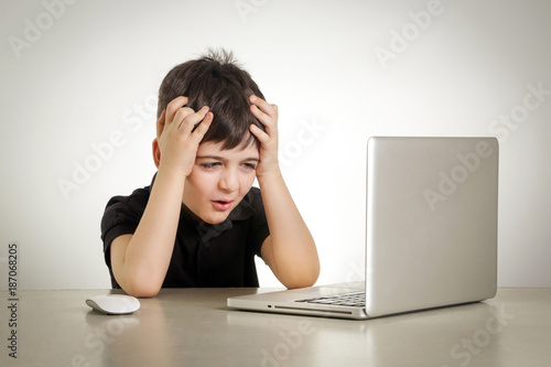 Studio portrait of schoolboy with headache in front of laptop