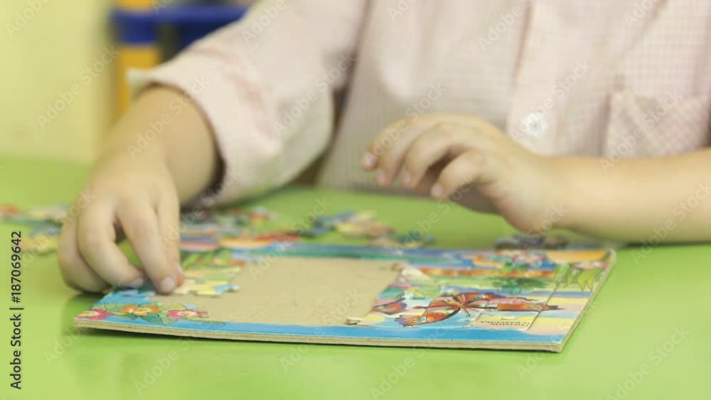 Close-up of hands of little unidentified child collecting picture from puzzles at the table in kindergarten Close-up of hands of little unidentified child collecting picture from puzzles at the table in kindergarten