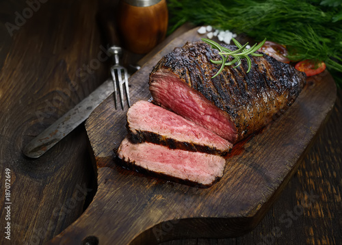 grilled steak with rosemary on a cutting board on a black background