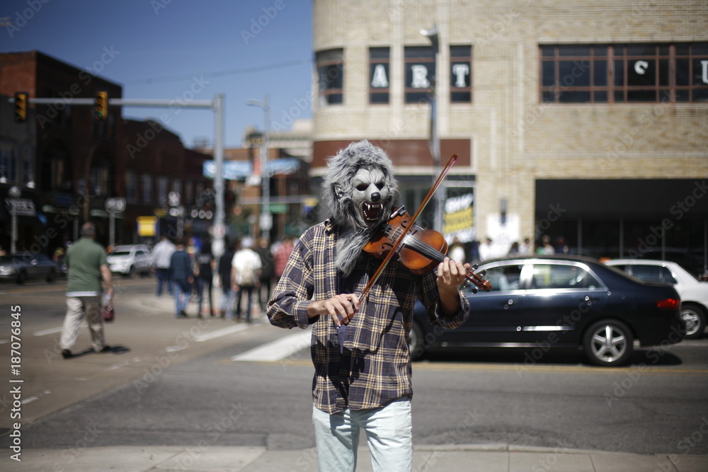 Obraz premium Man in a wolf mask playing violin downtown in front a city scene with word art above head.