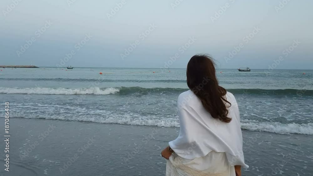 back view of young beautiful asian female standing on the beach and wind blow her hair while she is looking to the seascape and skyscape in the evening at dusk. relaxation, lifestyle, travel concept. back view of young beautiful asian female standing on the beach and wind blow her hair while she is looking to the seascape and skyscape in the evening at dusk. relaxation, lifestyle, travel concept.