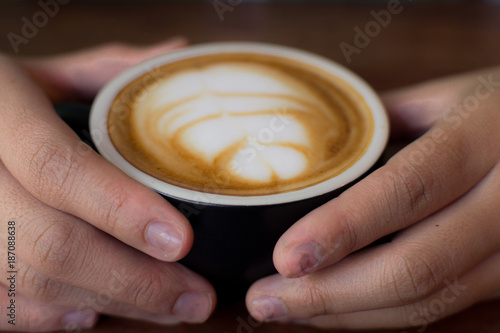 Close up Latte Art, Coffe cup latte art, Close up Hand of women holding a black cup of hot latte on wooden table. Close up woman hand holding cup of coffee in the cafe, vintage tone.