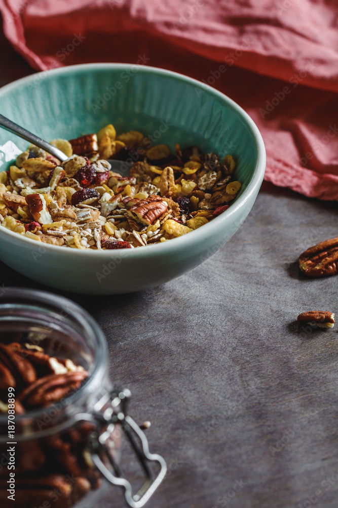 Fototapeta premium Muesli with dried berries and pecan nuts in ceramic bowl. Close-up of breakfast table.