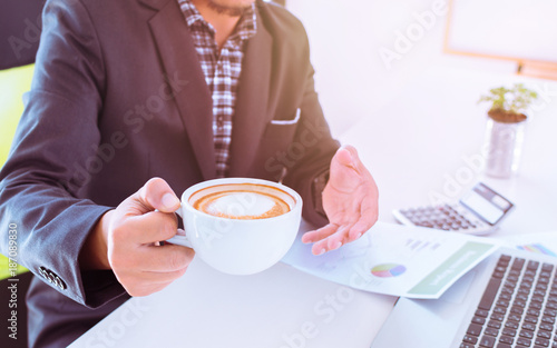 Businessmen are relaxing with coffee while using smart phone in the workplace. Business people are relaxing at the desk with a cup of coffee.