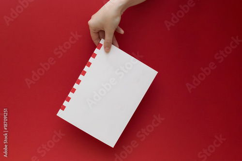 Female hand holding white sketchbook with red stripes on the plain red background