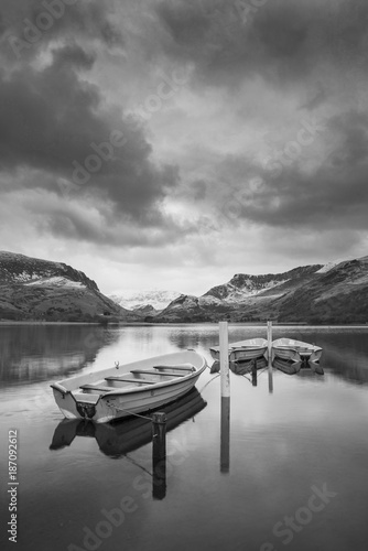 Beautiful black and white Winter landscape image of Llyn Nantlle in Snowdonia National Park with snow capped mountains in background