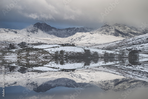 Beautiful Winter landscape image of Llynnau Mymbyr in Snowdonia National Park with snow capped mountains in background