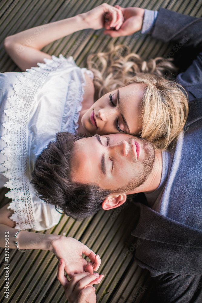Obraz premium Portrait of the young charming couple in love who lying head to head with closed eyes outdoor and holding hands each other