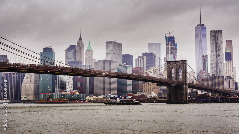 Fototapeta premium Manhattan and Brooklyn Bridge, New York City. Fast clouds float over the skyscrapers, cloudy weather, heavy traffic on the river