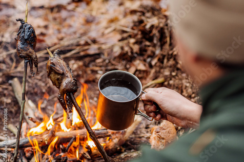 man traveler hands holding mug with water near the fire outdoors.