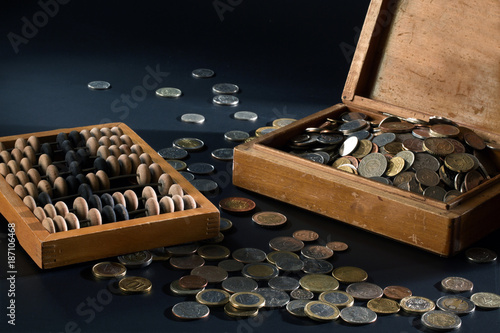 A pile of coins in a box and wooden abacus
