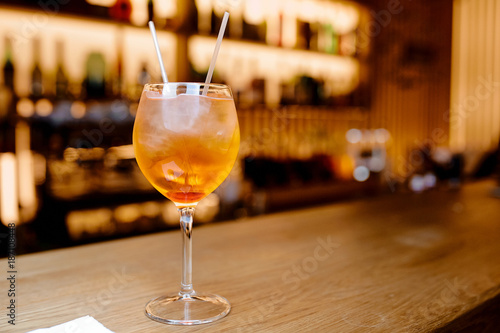 A refreshing Aperol Spritz cocktail with ice and a cherry on a wooden bar counter