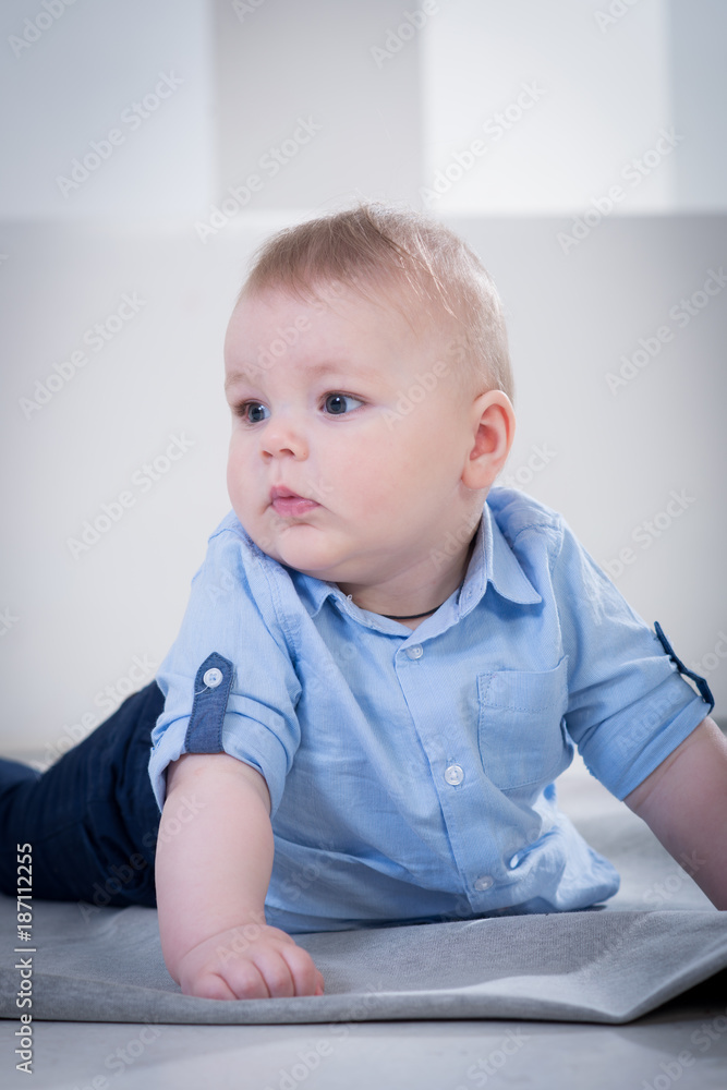 Cute little baby boy in blue shirt and jeans lying on the blanked and posing in the photo studio on white background Cute little baby boy in blue shirt and jeans lying on the blanked and posing in the photo studio on white background