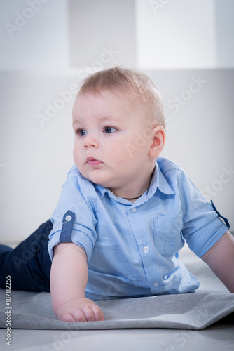 Cute little baby boy in blue shirt and jeans lying on the blanked and posing in the photo studio on white background