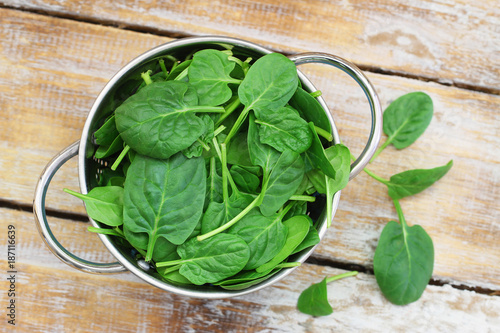Baby spinach leaves in colander on rustic wooden surface
